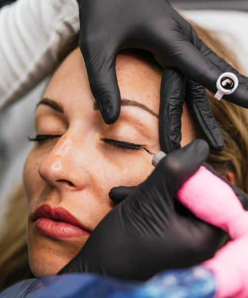 Closeup view of a professional cosmetic procedure, applying permanent eyeliner through micropigmentation on a woman’s eyelids in a beauty clinic Professional eyeliner micropigmentation procedure by a skilled beautician using precision application techniques and disposable gloves for safety and hygiene in a cosmetic tattooing clinic